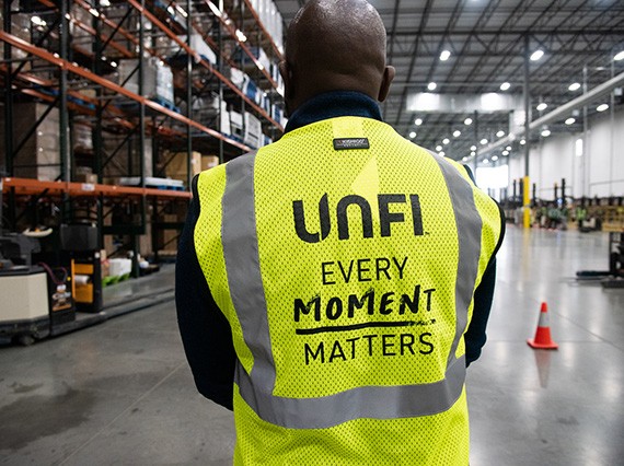 Back of UNFI warehouse worker in safety vest with the words "Every Moment Matters" printed on back.